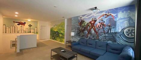 A modern living room with a blue sofa, a coffee table, a mural with superheroes, and a white reception desk.