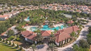 Un barrio residencial con piscina, palmeras y casas con techos de tejas rojas.