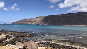 A coastal landscape with clear blue waters, rocky shore, and a large cliff.