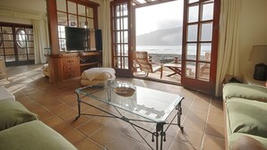 A living room with a glass coffee table, a television, and a view of the ocean through large windows.