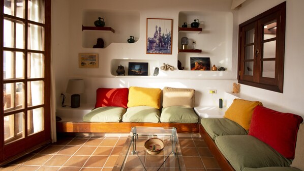Un salón con sofá, una mesa de centro de vidrio y una ventana con persianas.