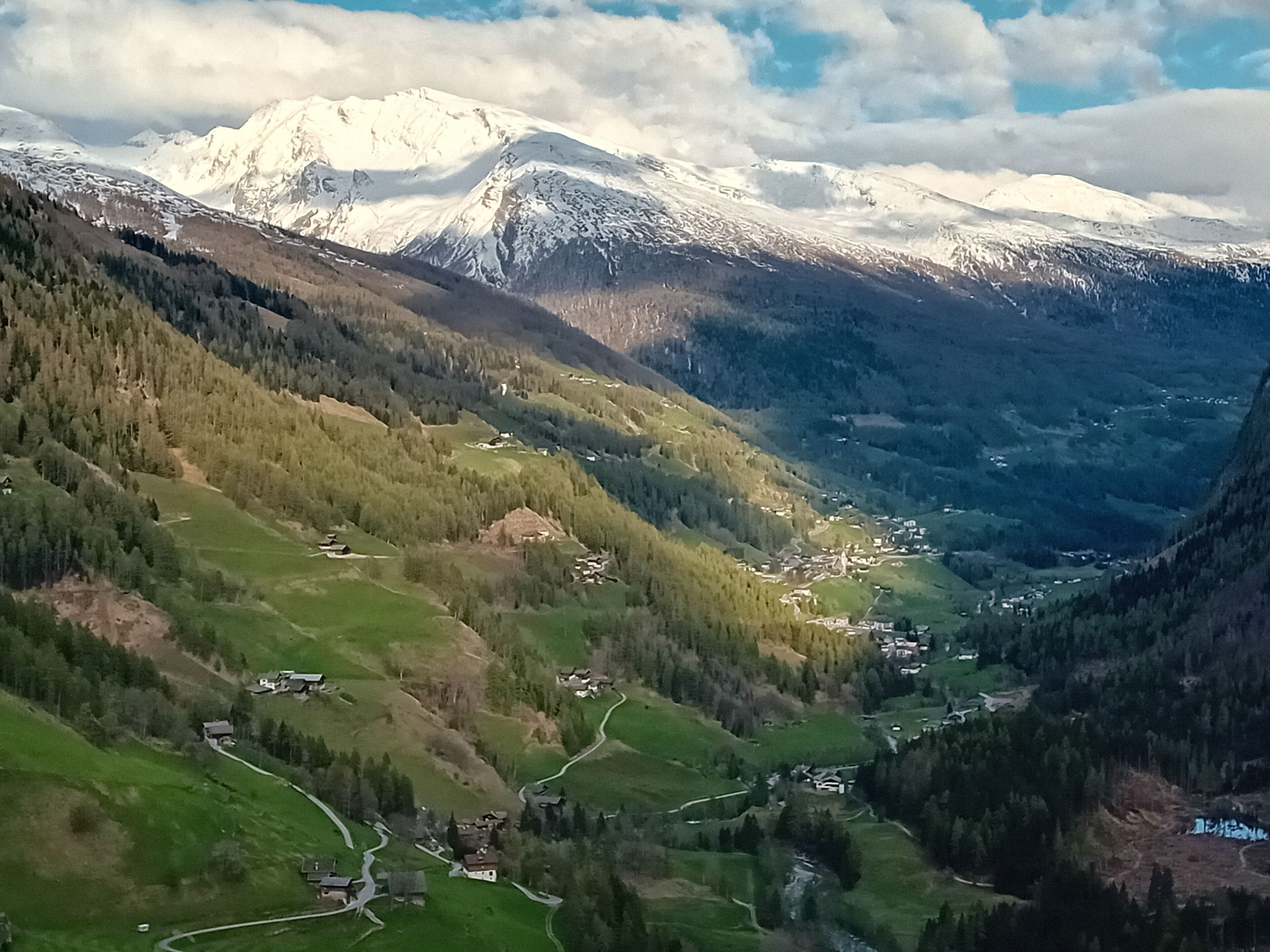 Eine gebirgige Landschaft mit schneebedeckten Gipfeln, grünen Tälern und verstreuten Häusern.