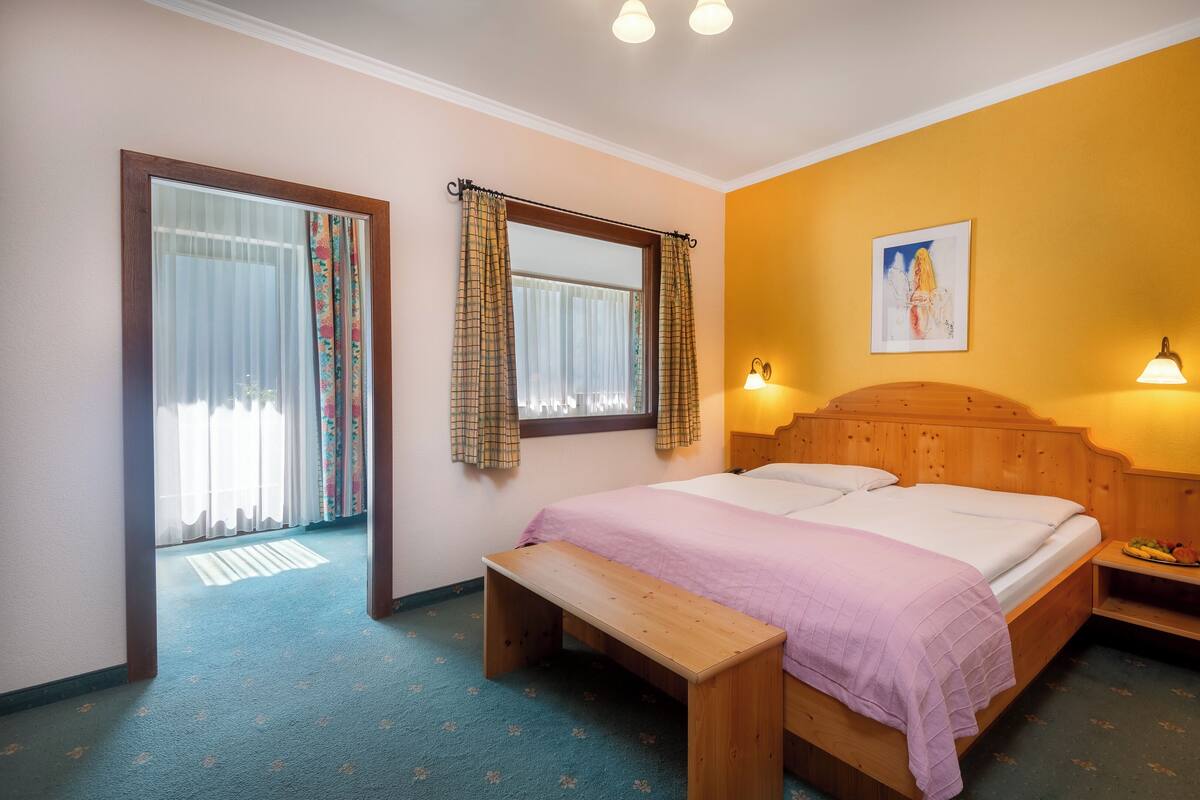 Un dormitorio con cama, banqueta, mesita de noche y una lámpara de pared.
