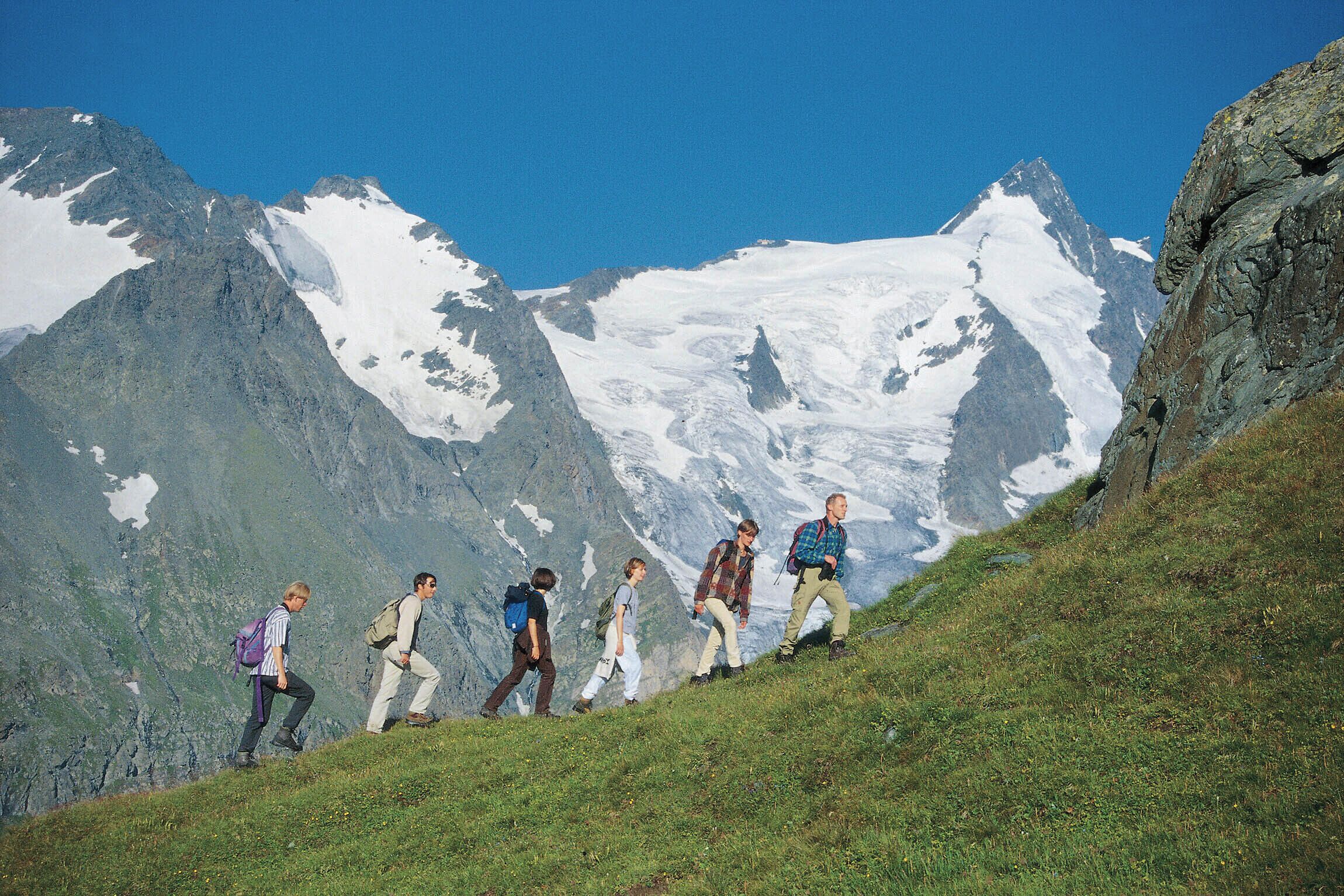 A group of hikers ascending a grassy slope with a mountainous backdrop.