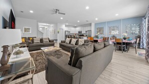 A modern living room with a sofa, coffee table, and decorative items. A dining area with a table and chairs is visible in the background. - Last Minute Disney! Private Pool, Hot Tub, Game Room & Themed Bedrooms. Book Now! #113675 (Orlando)