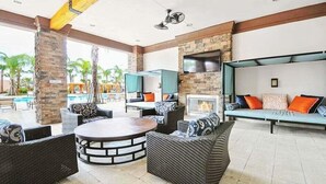 A spacious outdoor lounge area with wicker furniture, a round table, and a stone fireplace. - Last Minute Disney! Private Pool, Hot Tub, Game Room & Themed Bedrooms. Book Now! #113675 (Orlando)