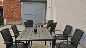 A patio with a rectangular table and six chairs, a grey double door, and a brick wall. - Schöne Groß Ferienwohnung 78m² Ideal für Familie 3 Schlafzimmer Zentrumnah 1.og (Erfurt)