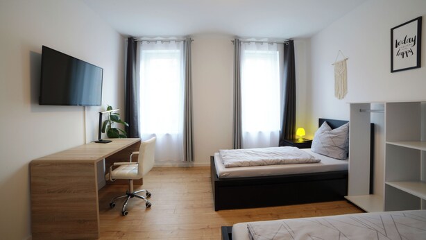 A modern bedroom with a wooden desk, a bed, and a TV mounted on the wall. - Schöne Groß Ferienwohnung 78m² Ideal für Familie 3 Schlafzimmer Zentrumnah 1.og (Erfurt)