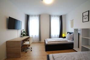 Um quarto moderno com escrivaninha de madeira, uma cama e uma TV fixada na parede.