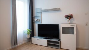 A modern living room with a flat-screen TV, a small plant, and a decorative vase on a white cabinet. - Schöne Groß Ferienwohnung 78m² Ideal für Familie 3 Schlafzimmer Zentrumnah 1.og (Erfurt)