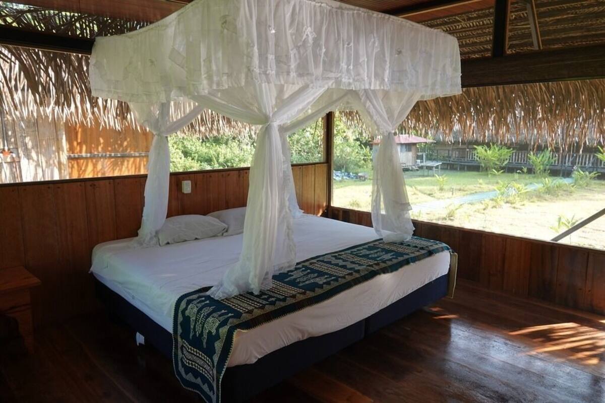 Uma cama com dossel, paredes de madeira e vista para um jardim.