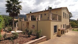 A two-story building with a balcony, a garden with a statue, and a palm tree. - Villa in Nature with Yoga Room, Peace and Tranquility (Puigpuñent)