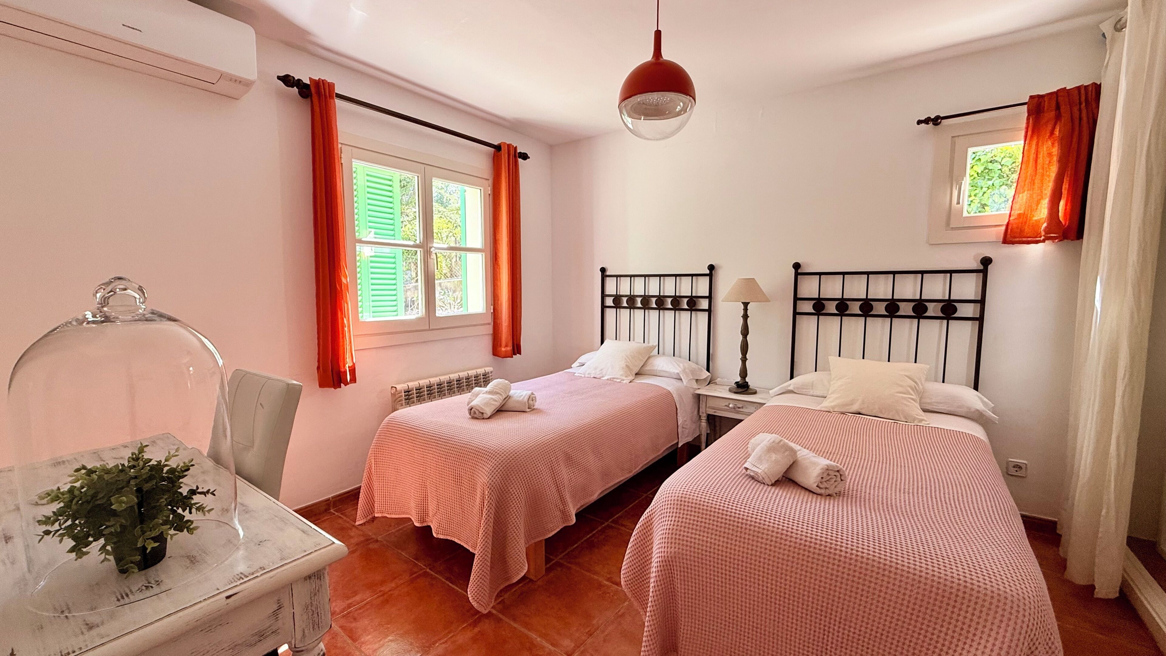 A bedroom with two single beds, a bedside table with a lamp, a chair, a radiator, and a window with curtains.