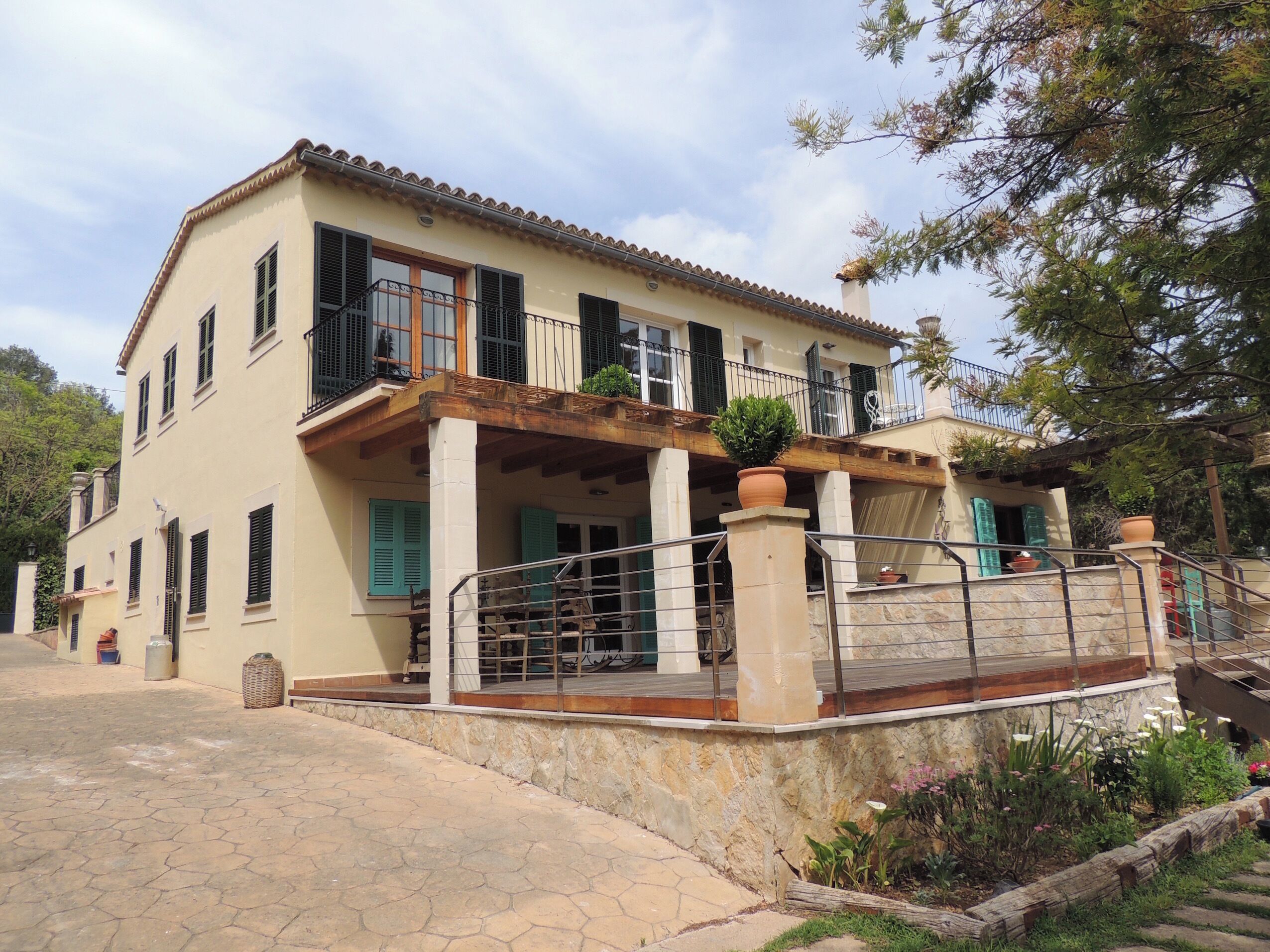 A two-story house with a balcony, a stone pathway, and a garden area.