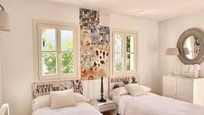 A bedroom with two beds, a wall with pictures, a window, and a mirror. - Villa in Nature with Yoga Room, Peace and Tranquility (Puigpuñent)