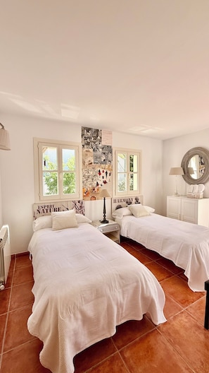Un dormitorio con dos camas, una pared decorada con cuadros, una ventana y un espejo.