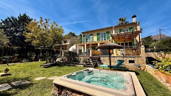 A two-story house with a hot tub in the backyard, a staircase, and a patio area.