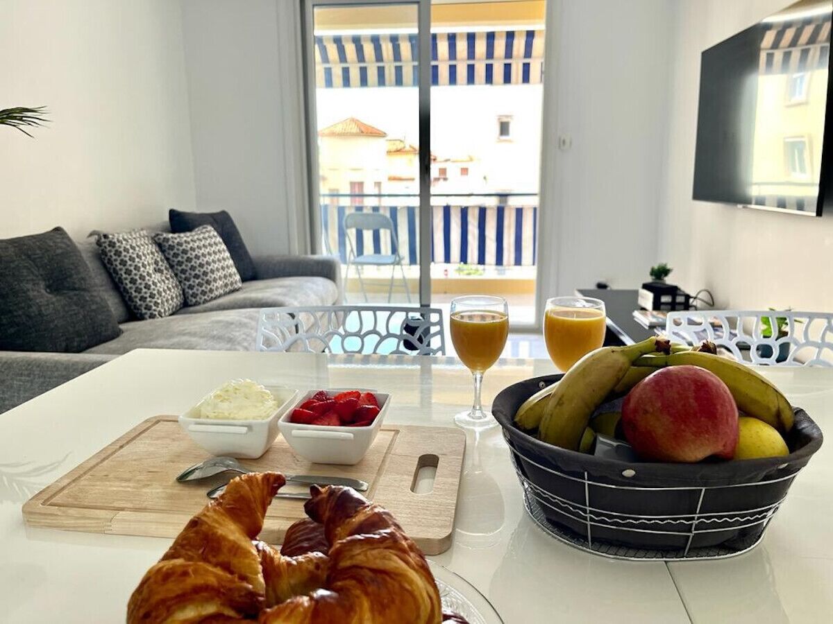 Frühstücksaufbau mit Croissants, Obst und Saft auf einem Balkon mit Blick auf Gebäude.