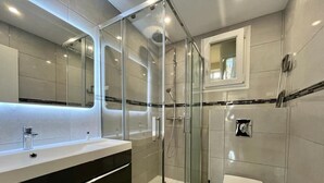 A modern bathroom with a glass-enclosed shower, a white toilet, and a vanity with a mirror. - Apartment 3 bedrooms 3 min to beach (Cannes)