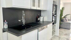 A modern kitchen with a black countertop, stainless steel appliances, and white cabinetry. - Apartment 3 bedrooms 3 min to beach (Cannes)