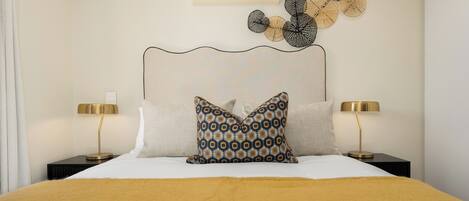 A neatly made bed with a patterned pillow, two bedside lamps, and a wall-mounted air conditioner.