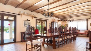 A spacious dining area with a long wooden table and chairs, a chandelier, and a view of the outdoors. - Holidays in Portocolom at Finca Casa Toni Diaz (Felanitx)