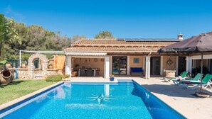 A swimming pool with a tiled deck, a covered patio area with lounge chairs, and a stone archway. - Holidays in Portocolom at Finca Casa Toni Diaz (Felanitx)