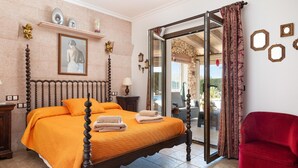A bedroom with a bed, a red chair, a glass door leading to an outdoor area, and a stone wall with decorative items. - Holidays in Portocolom at Finca Casa Toni Diaz (Felanitx)