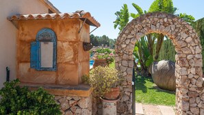 A rustic building with a stone archway, a small window with blue shutters, and a garden with potted plants and a large rock. - Holidays in Portocolom at Finca Casa Toni Diaz (Felanitx)