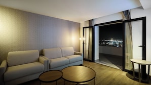 A modern living room with a sofa, two small tables, and a view of the city at night through a glass door.