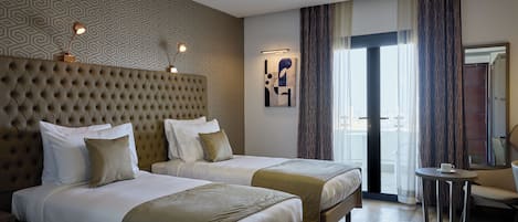A hotel room with two beds, a tufted headboard, a patterned wall, a painting, and a view of the outdoors through a door.