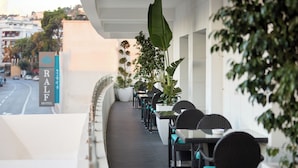 A hotel balcony with outdoor seating, a sign for the Ralf Hotel, and a view of the street and buildings in the background.