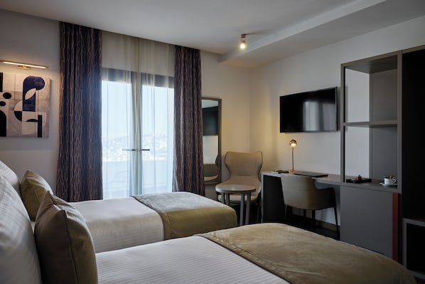 A hotel room with two beds, a desk, a chair, a TV, and a large window with curtains. - Hôtel RALF (Algiers)