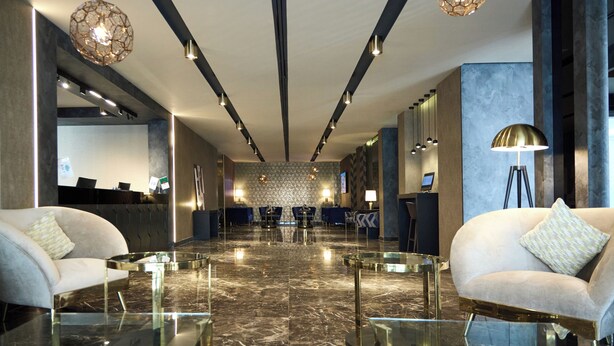A modern lobby with marble flooring, two sofas, a reception desk, and a patterned wall.