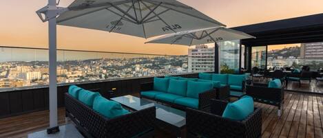 A rooftop terrace with outdoor seating, a large umbrella, and a city view.