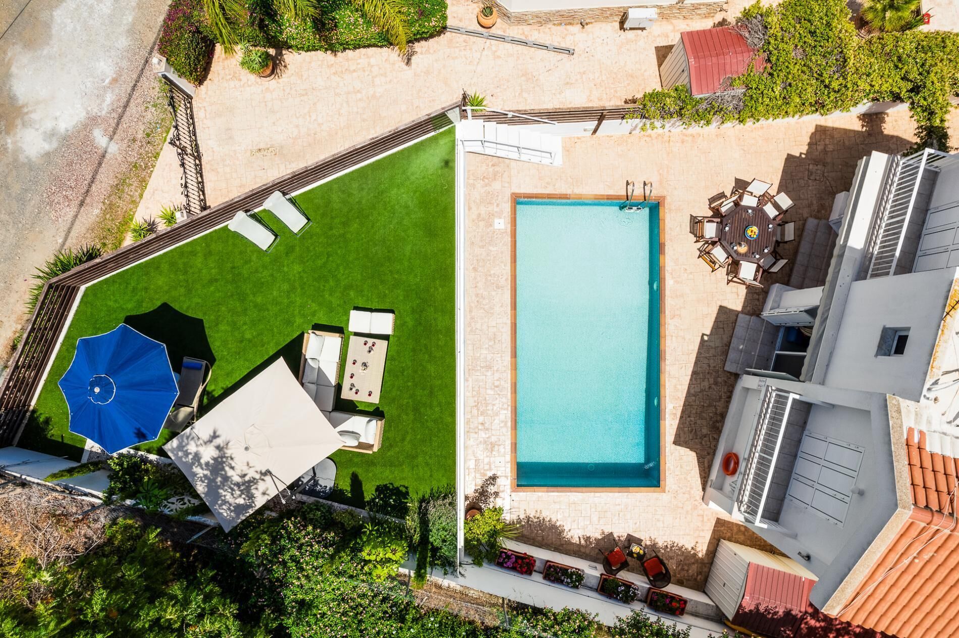 An aerial view of a backyard with a swimming pool, a patio with a table and chairs, and a small shed.