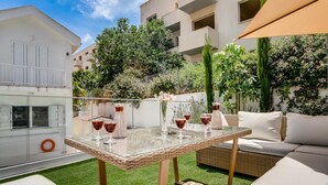 A glass-top table with wicker chairs and cushions, surrounded by greenery and a clear sky.