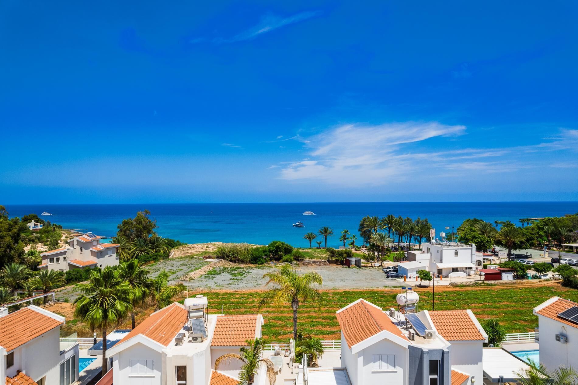 A coastal residential area with houses, a clear blue sky, and the sea in the background.