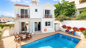 A two-story house with a swimming pool, outdoor furniture, and potted plants.