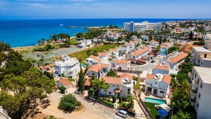 A coastal residential area with white buildings, a swimming pool, and a view of the sea.