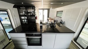 A modern kitchen with a central island, built-in appliances, and a dining area with a bench. - Island Harbour Houseboat (Binfield)