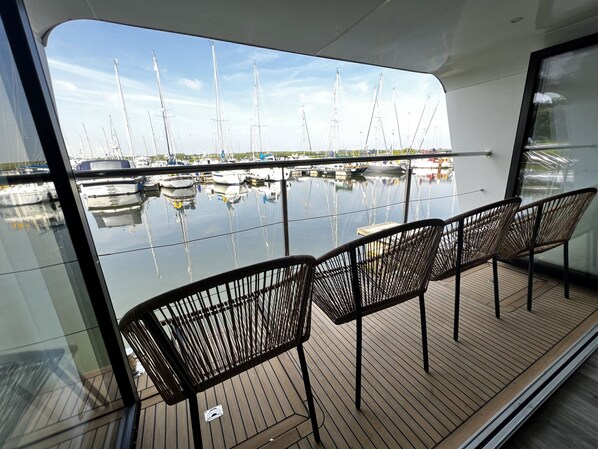 Terraza con cuatro sillas de mimbre y vista a un puerto deportivo con varios veleros.