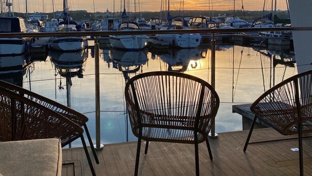 A view from a boat deck at sunset with several chairs and a table, overlooking a marina with multiple boats. - Island Harbour Houseboat (Binfield)