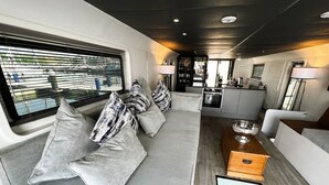 A modern interior with a sofa set, a wooden table, and a kitchen area. - Island Harbour Houseboat (Binfield)