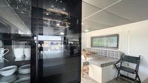 A compact kitchenette with a black refrigerator, a small dining table, and a bench. - Island Harbour Houseboat (Binfield)