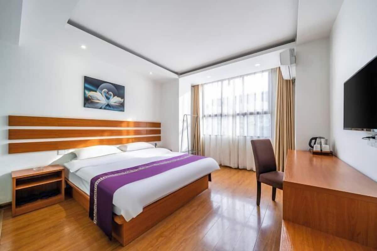 Habitación de hotel con cama de madera, un escritorio, una silla, un televisor y un cuadro en la pared.
