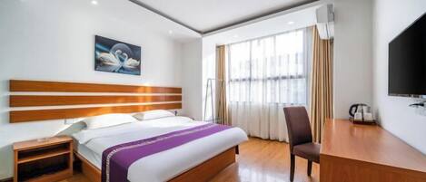 A hotel room with a wooden bed, a desk, a chair, a TV, and a painting on the wall.