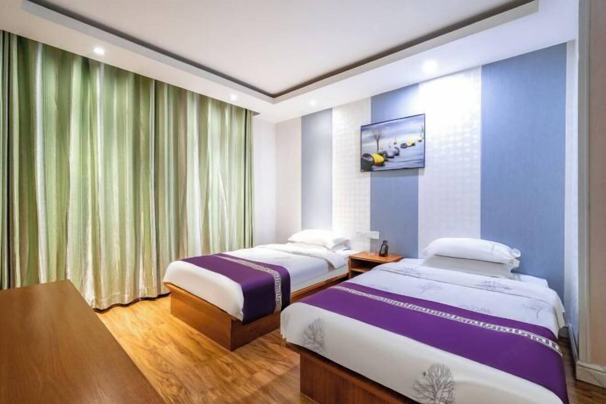 Habitación de hotel con dos camas, un escritorio de madera y un ventanal con cortinas.