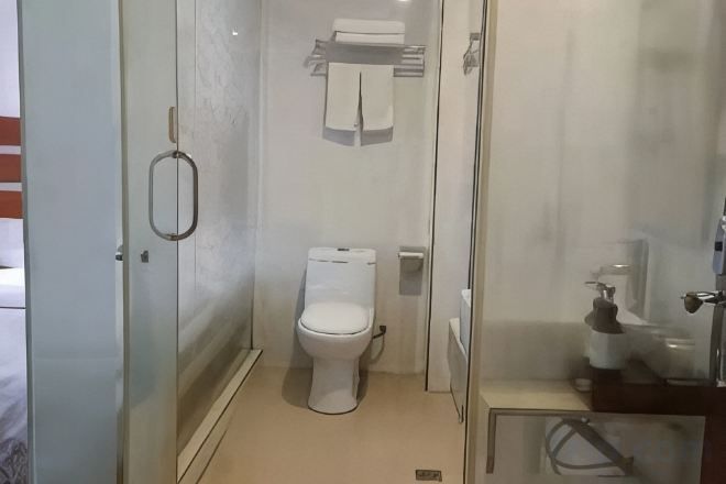 Un baño con inodoro, cabina de ducha de vidrio y lavamanos con dispensador de jabón.