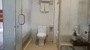 Un baño con inodoro, cabina de ducha de vidrio y lavamanos con dispensador de jabón.